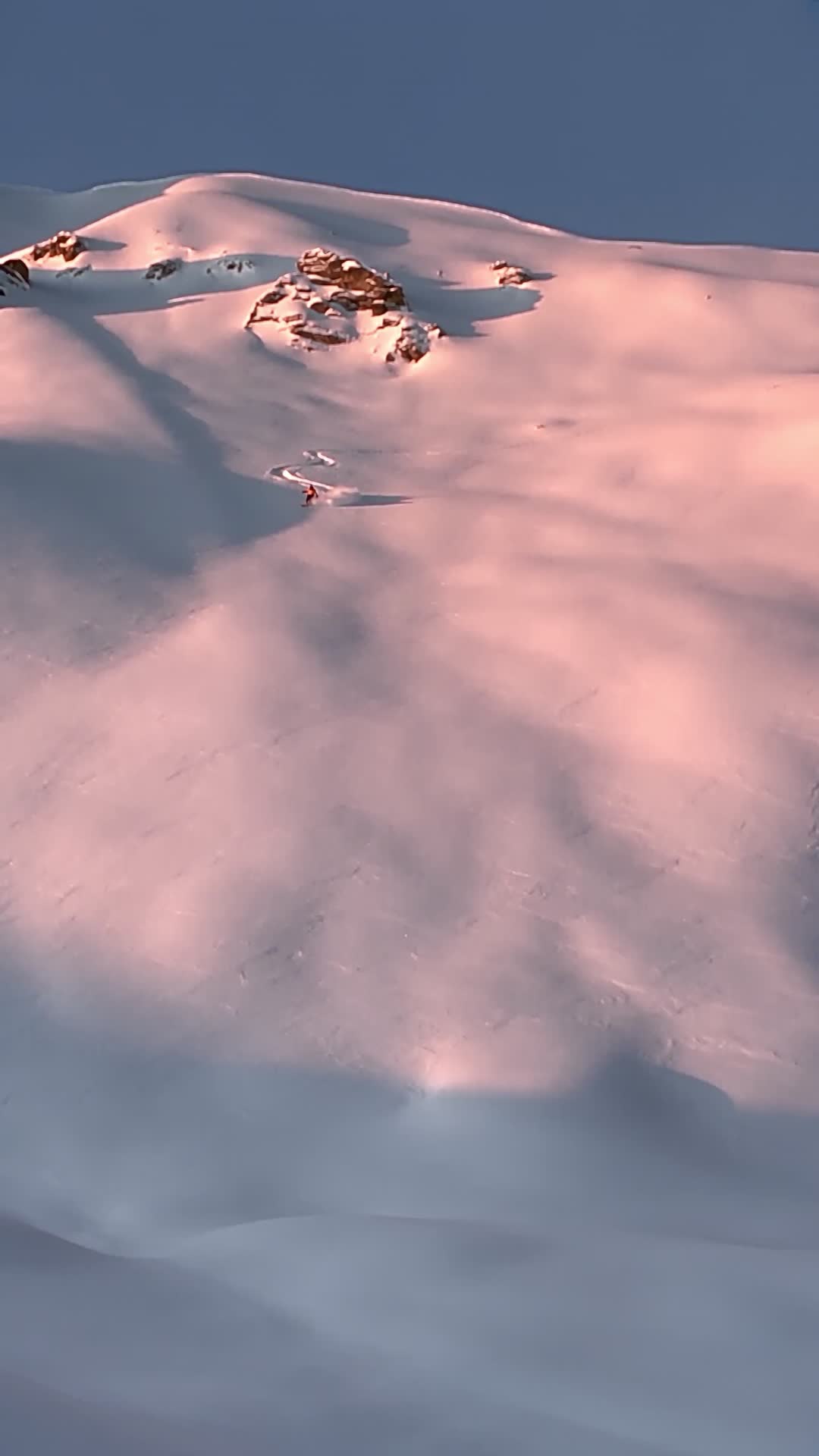 Skier Carving Down Untouched Snow Slope at Sunset
